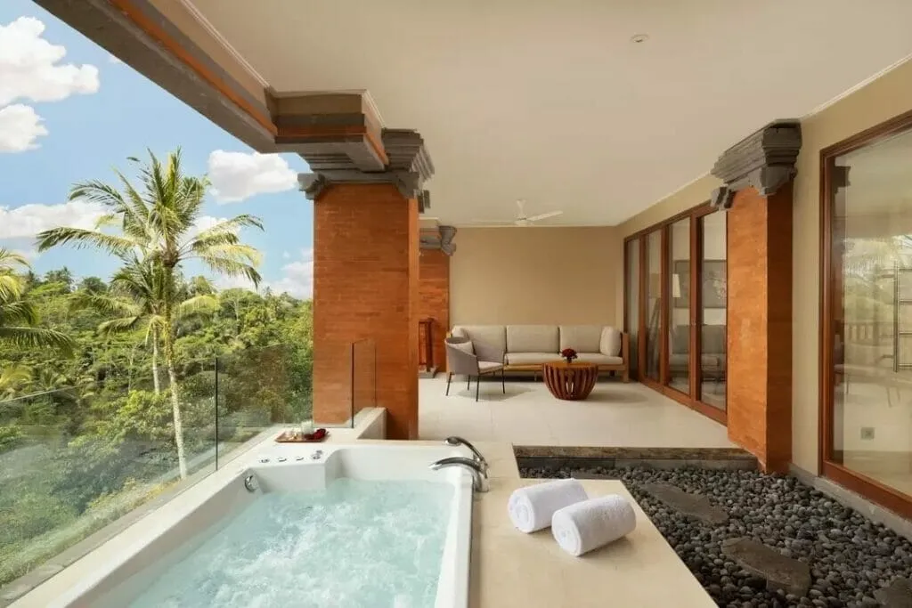 Padma Resort'a ait, palmiye ağaçları ve tropikal orman manzarasına bakan, köpüklü suya sahip şık bir jakuzi ile modern oturma grubunun bulunduğu geniş ve lüks bir balkon veya teras alanı.