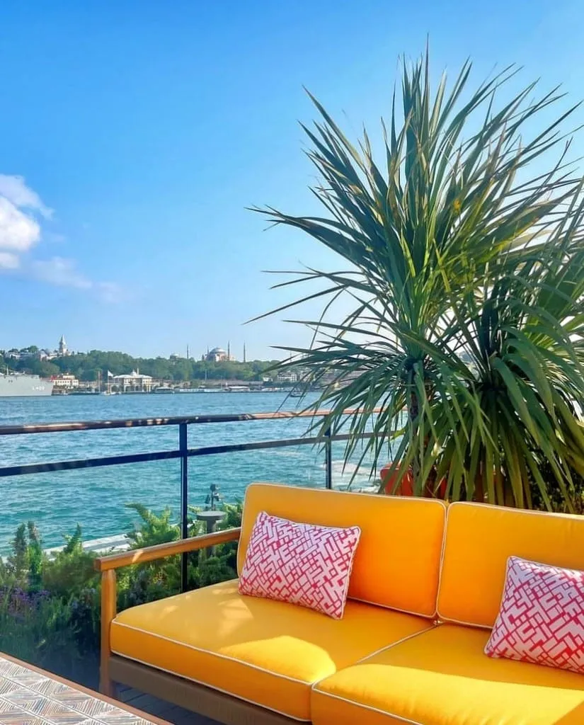 Sail Loft’un terasında, sarı minderli rahat koltuk ve arka planda Boğaz manzarasıyla keyifli bir oturma alanı.