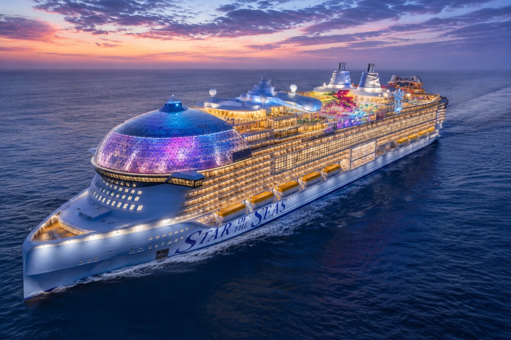 Günbatımı kızıllığında denizde süzülen, Royal Caribbean'ın ultra lüks Star of the Seas kruvaziyer gemisi, önündeki mor ve mavi ışıklarla aydınlatılmış görkemli cam kubbesi, ışıl ışıl katları ve renkli su kaydıraklarıyla unutulmaz bir cruise tatili deneyimi sunuyor.