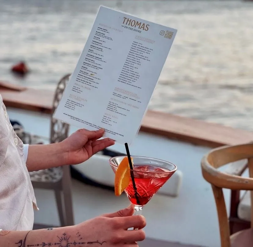 Thomas On the Shore menüsü ve kırmızı kokteyl, Boğaz manzarası eşliğinde sunuluyor.