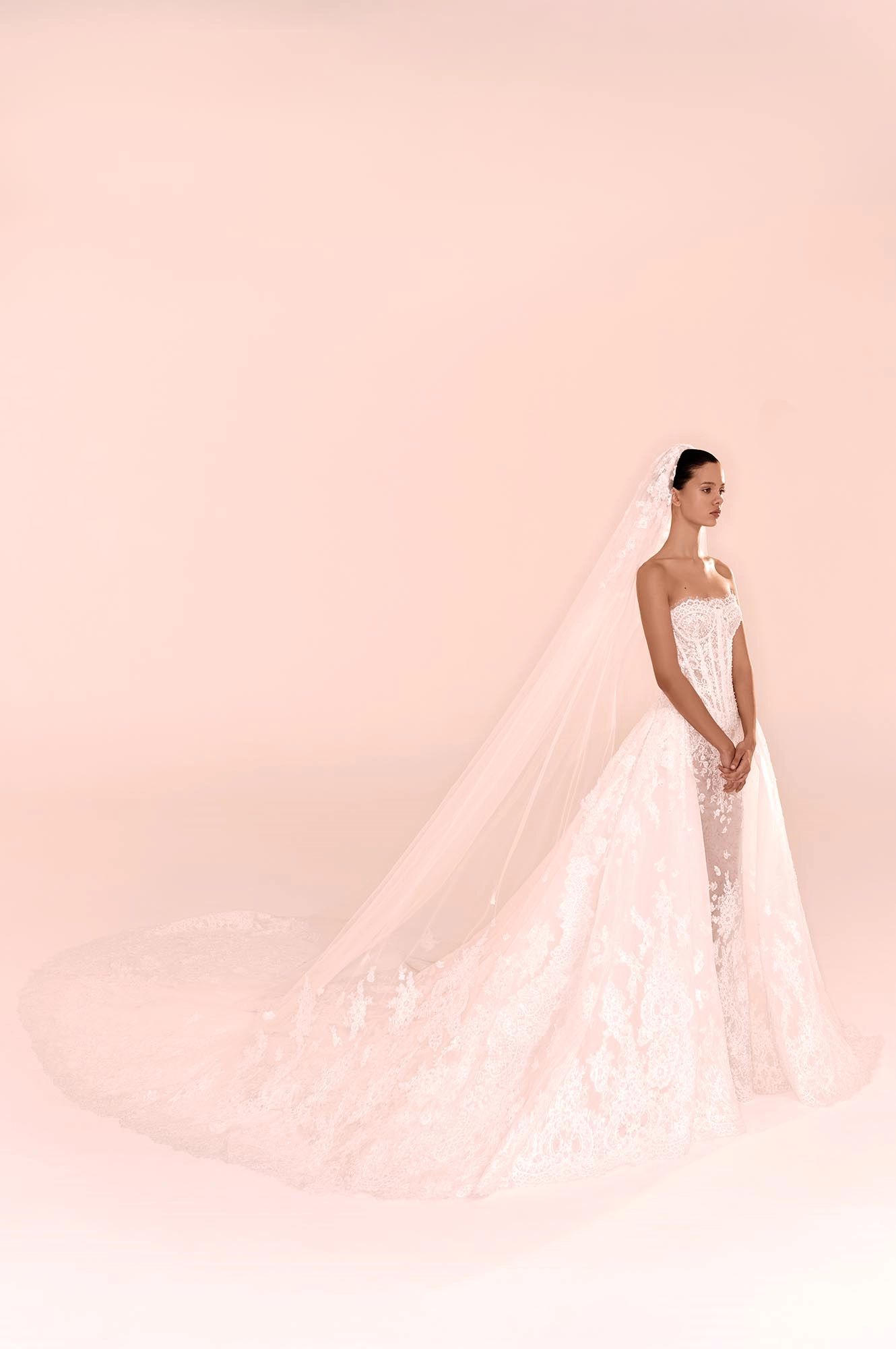 Zuhair Murad'ın 2025 Sonbahar gelinlik koleksiyonundan, transparan detaylara sahip, tüm bedeni saran zarif dantel işlemelerle süslü straplez korseli, katmanlı hacimli eteği ve uzun kuyruğuyla romantik bir siluet sunan etkileyici bir gelinlik.