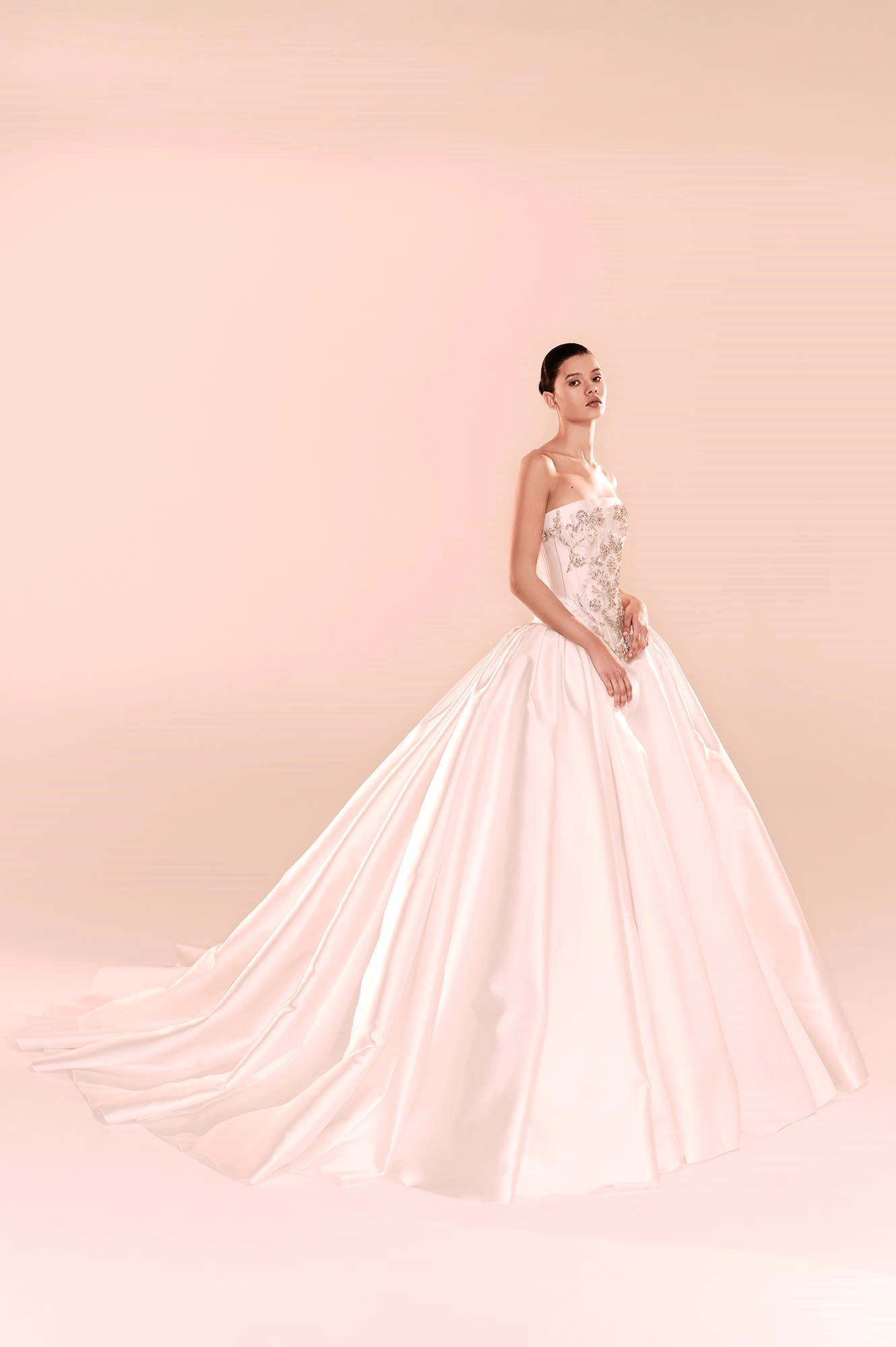Modelin zarif bir duruşla poz verdiği bu Zuhair Murad gelinlik, gümüş ipliklerle işlenmiş ışıltılı korsajı ve yere kadar uzanan kabarık eteğiyle couture işçiliğinin romantik bir yorumunu sunarak 2025 Sonbahar gelinlik modelleri arasında göz kamaştırıyor.