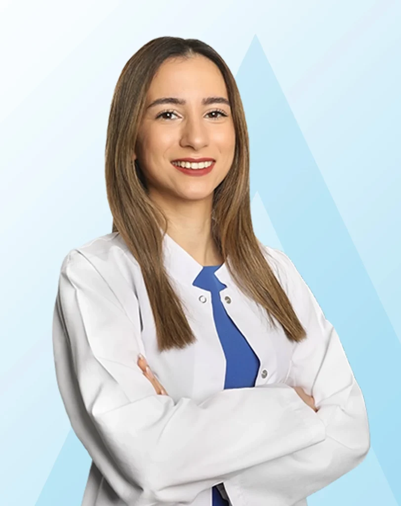 Acıbadem Taksim Hastanesi Beslenme ve Diyet Uzmanı Bensu Enyüksek, bağışıklık sistemini güçlendirmenin yolları hakkında bilgi veren makalede, beyaz önlüğü ve mavi bluzuyla kolları bağlı, güler yüzlü bir şekilde kameraya bakıyor.