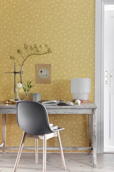 Sarı desenli duvar kağıdı ile canlılık katılmış bir home office alanı; gri sandalye ve eskitme ahşap masa ile tamamlanmış yaratıcı bir atmosfer.