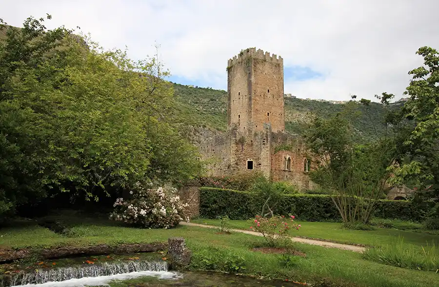 Giardino di Ninfa'nın yemyeşil doğasında, eski bir manastırın kalıntıları üzerine kurulmuş tarihi taş kule ve harabeler, gür ağaçlar, çiçekli çalılar, çimenlik bir yol ve berrak bir akarsu ile çevrili huzurlu bir manzara sunarak Roma seyahati sırasında keşfedilebilecek dingin bir kaçış noktası.