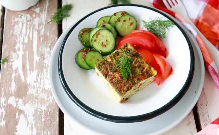 Beyaz tabakta sunulan ketojenik kahvaltı: kabaklı fırın omlet dilimi, dilimlenmiş salatalık ve domates eşliğinde, dereotu ile süslenmiş sağlıklı ve düşük karbonhidratlı bir öğün.