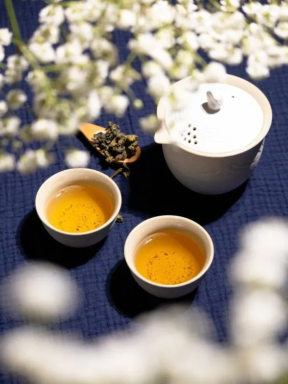 Seramik demlik ve fincanlarda sunulan klasik oolong çayı; beyaz çiçekler eşliğinde huzurlu bir çay seremonisi.