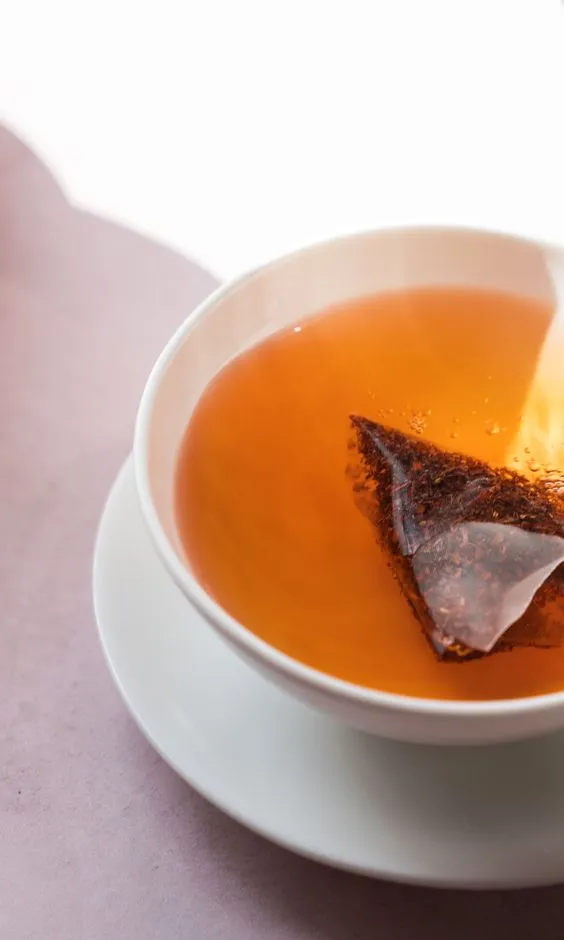 Üçgen poşet içinde demlenen amber renkli rooibos çayı, beyaz fincan içinde servis ediliyor.