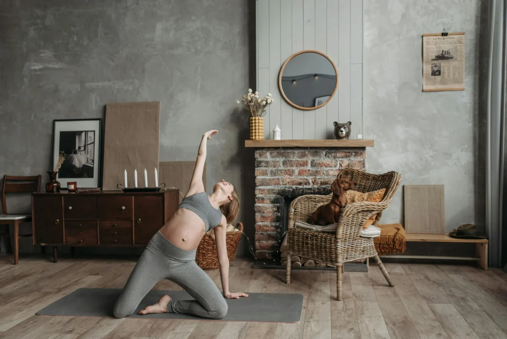Hamile bir kadın evinde yoga yaparken, yanında koltukta dinlenen köpeğiyle birlikte dengeli, sağlıklı ve sürdürülebilir bir yaşam tarzını simgeliyor.