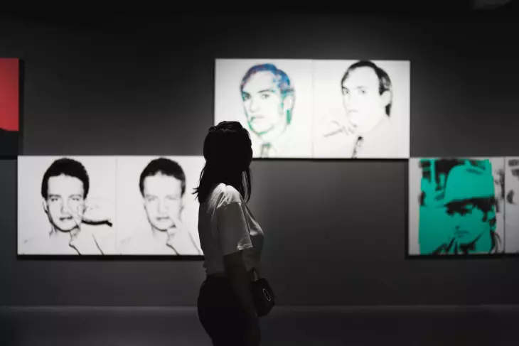 Siyah beyaz ve renkli serigrafi portrelerinden oluşan sergiyi inceleyen kadın ziyaretçi.