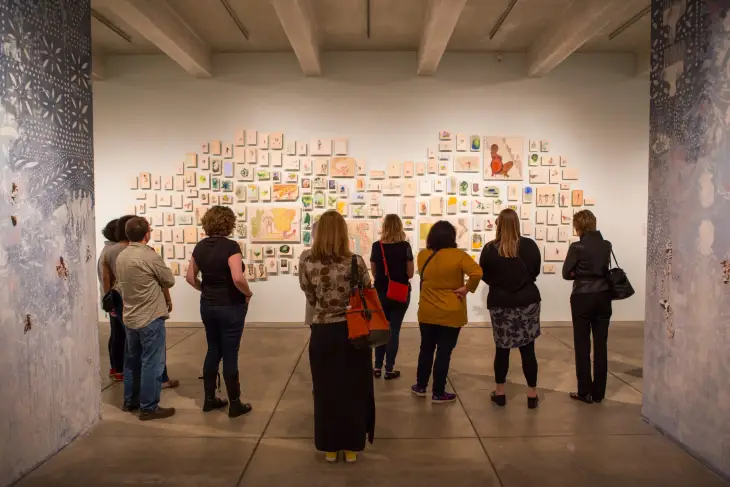 Andy Warhol Müzesi’nde izleyicilerin dikkatle incelediği çok parçalı duvar enstalasyonu; sanatseverlerle dolu bir galeri deneyimi.