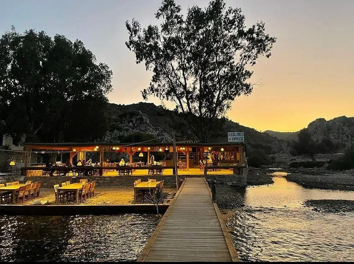 Yat turu için uygun olan Bozukkale'deki Sailors House restoranı, gün batımının altın rengi ışıkları altında, suya uzanan ahşap iskelesi ve içinde ile dışarıda parlayan aydınlık masalarıyla, tepelerle çevrili bir koyda huzurlu bir yemek deneyimi vaat ediyor.