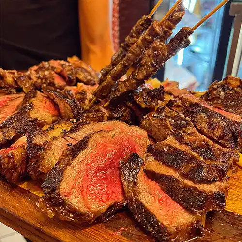 Roma Seyahat Rehberi'nin gastronomi bölümünde öne çıkan Bufalero restoranının sunumuyla, mükemmel bir şekilde pişirilmiş, ortası sulu pembe, kenarları çıtır mühürlenmiş, üzerinde iri tuz taneleri parlayan et dilimleri ve yanında servis edilen çöp şişlerin yer aldığı bu enfes kare, şehrin zengin lezzet duraklarından sadece birine davet ediyor.