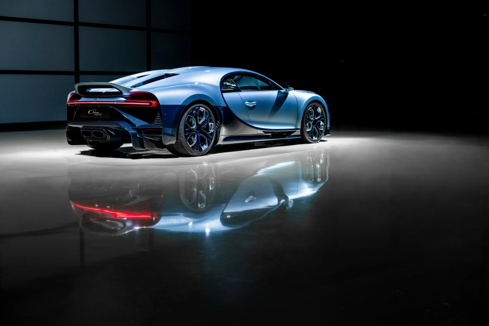 Arka üç çeyrek açıdan, şık bir stüdyo ortamında parlak zeminde duran, mavi ve koyu karbon fiber detaylara sahip Bugatti Chiron Profilee hiper otomobil, güçlü arka tasarımıyla dünyanın en pahalı arabaları arasındaki yerini sergiliyor.