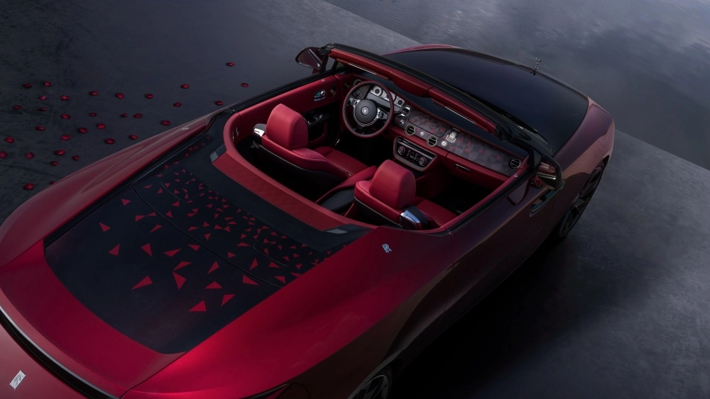 Kırmızı koltuklu ve iç mekana sahip Rolls-Royce La Rose Noire Drop Tail adlı lüks üstü açık otomobilin tepeden çekilmiş bu görselinde, arka bölümdeki siyah paneli süsleyen kırmızı üçgen desenler ve etrafa serpilmiş gül yaprakları, dünyanın en pahalı arabası olan bu sınırlı üretim modelin özel atmosferini yansıtıyor.