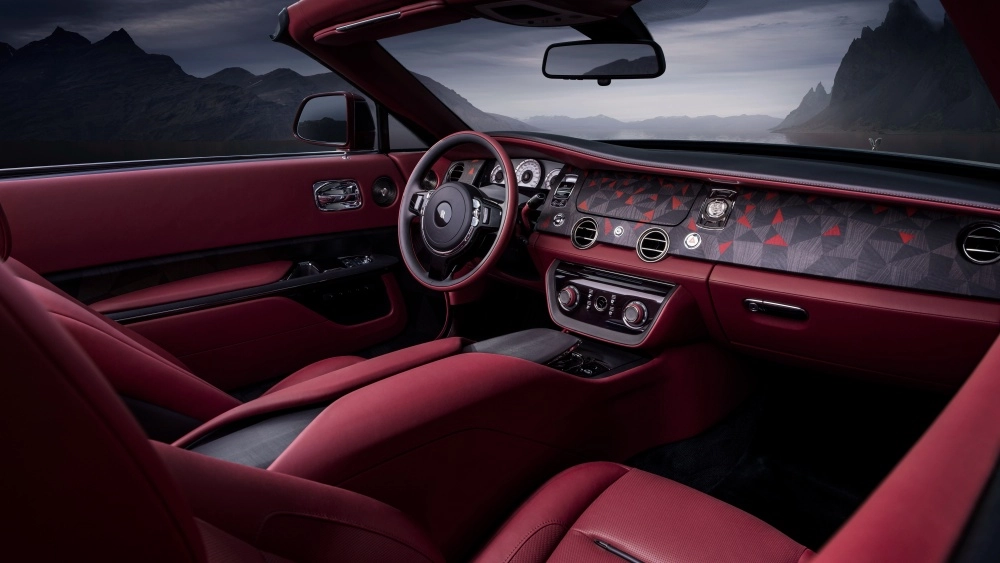 Dünyanın en pahalı arabası Rolls-Royce La Rose Noire Drop Tail'in lüks iç mekan tasarımı; koyu kırmızı deri koltukları, özgün geometrik desenlerle süslü gösterge paneli ve aracın açık tavanından görünen dramatik dağlık dış manzarasıyla dikkat çekiyor.