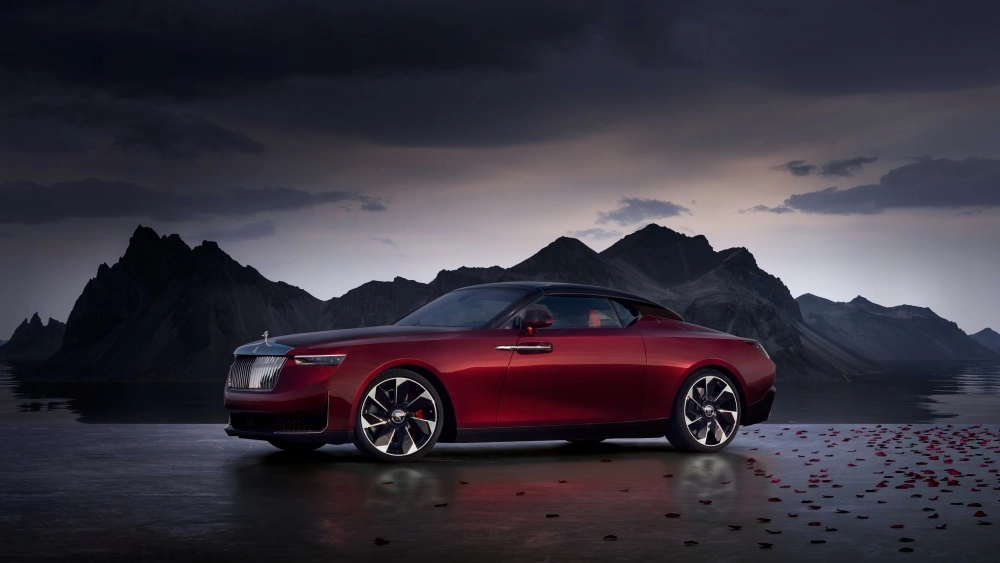 Görkemli dağlar ve dramatik bulutlu bir gökyüzü altında, suya yansıyan kırmızı gül yaprakları arasında konumlanmış, Rolls-Royce La Rose Noire Drop Tail modeli bu koyu kırmızı lüks otomobil, dünyanın en pahalı arabası olarak zarafetini sergiliyor.