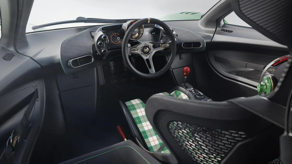 Gordon Murray S1 LM hiper otomobilin karbon fiber ağırlıklı, modern ve sporcu iç mekan tasarımında, merkezde konumlanmış direksiyon, dijital ekranlar, kırmızı vites topuzu ve yeşil ekoseli desenli yolcu koltuğu göze çarpıyor.