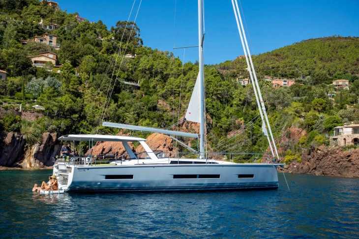 Yaz günü doğal koya demirlemiş gri renkli Hanse Yachts 590 modern yelkenli tekne ve arka platformunda güneşlenen insanlar
