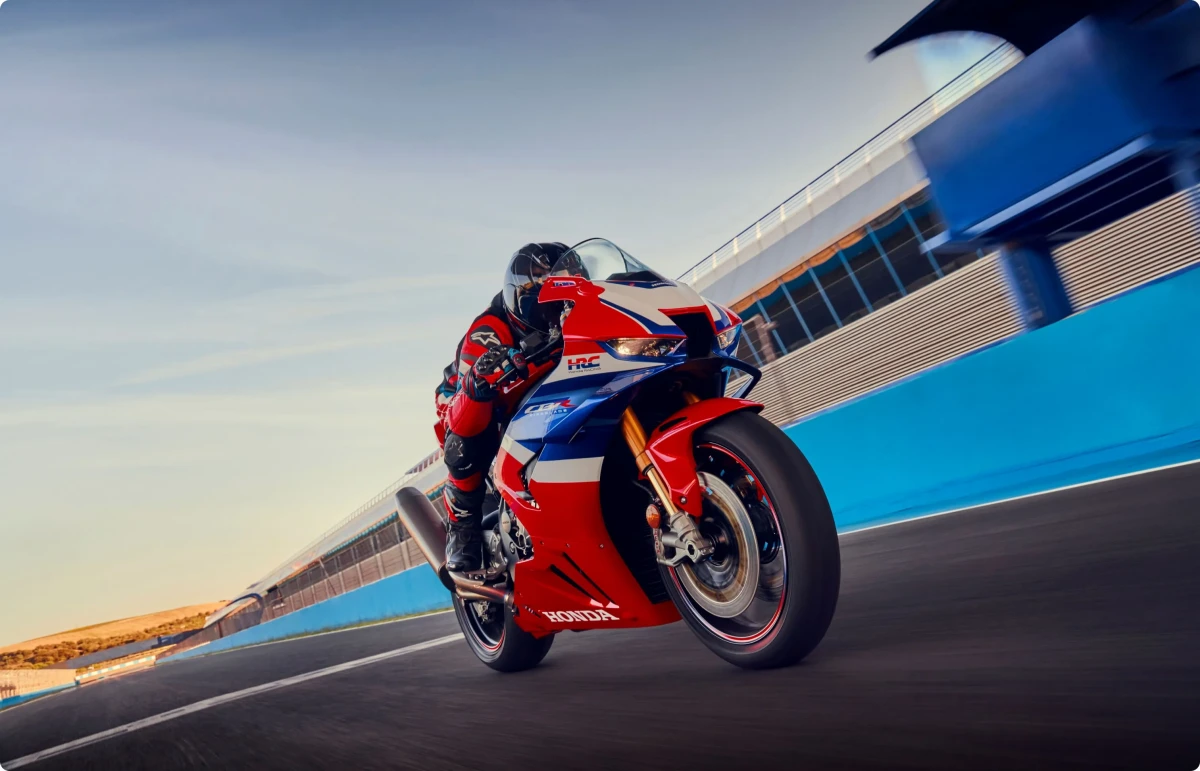 Kırmızı, beyaz ve mavi renkleriyle dikkat çeken Honda CBR1000RR-R Fireblade SP yarış motosikleti, uyumlu kırmızı-siyah tulumlu bir sürücüyle birlikte bir pistte yüksek hızda viraj alırken anlık bir karede yakalanmış.