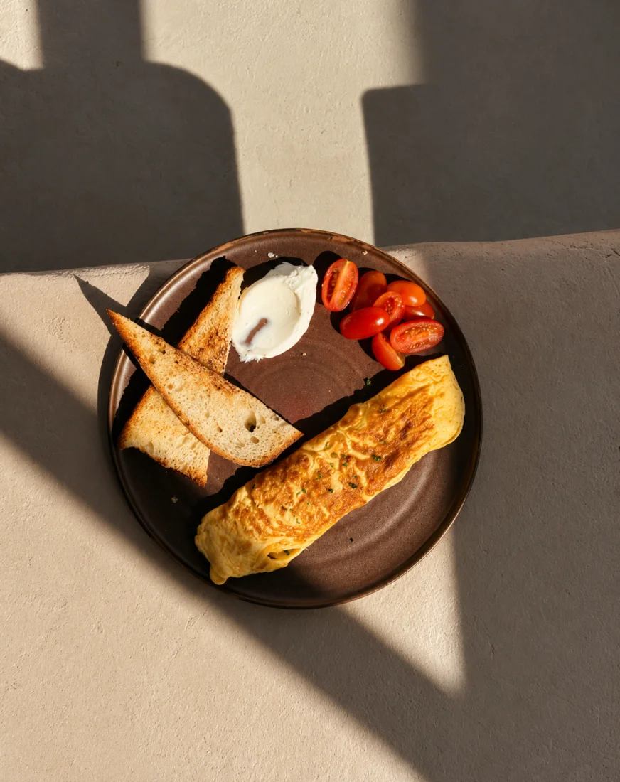 Latmos Athens’te güneş ışığı alan bir masada, kızarmış ekmek ve cherry domateslerle servis edilen omlet tabağı.