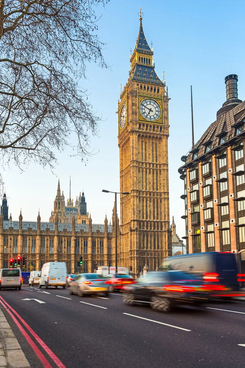 Mavi gökyüzü altında, Londra'nın sembolü Big Ben saat kulesi ve görkemli Parlamento Binası'nın önünden akan yoğun cadde trafiği, şehrin seyahat rehberindeki dinamik atmosferini yansıtıyor.