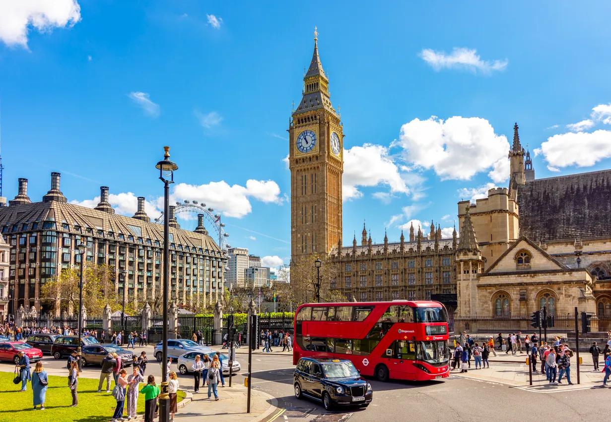 Güneşli bir havada, ikonik Big Ben'in görkemli duruşuyla Londra'nın tarihi Parlamento Binası, Portcullis House ve uzaktaki London Eye'ın görüldüğü hareketli caddede, kırmızı çift katlı otobüs ve siyah taksilerle birlikte keyifli bir gün geçiren çok sayıda insan Londra seyahatinin canlılığını yansıtıyor.