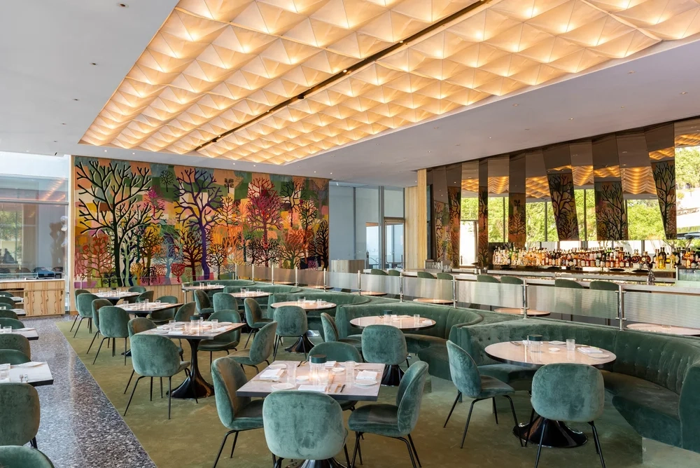 Houston Güzel Sanatlar Müzesi'ndeki Le Jardinier müze restoranının, doğadan ilham alan zarif bir atmosfer sunan iç mekânı; yeşil kadife oturma grupları, özenle hazırlanmış masalar, canlı renklerde ağaç motifli duvar panosu ve aydınlatmalı geometrik tavanıyla dikkat çekiyor.