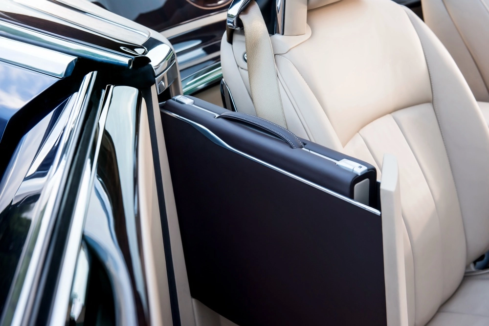 Rolls-Royce Sweptail'in bej deri koltuğunun yanında, özenle yerleştirilmiş, el işçiliği ile tasarlanmış, krom detaylı siyah bir özel üretim bavul bölmesi belirginleşiyor, aracın eşsiz iç mekan detayını ve limitli üretim lüksünü vurguluyor.
