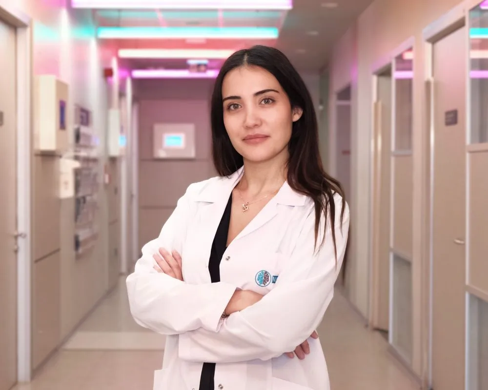 NPİSTANBUL Hastanesi'nden bir uzman klinik psikolog, aydınlık hastane koridorunda beyaz önlüğüyle kollarını kavuşturmuş bir şekilde kameraya bakarak kaliteli uyku ve daha iyi dinlenmek için bilim destekli öneriler sunuyor.