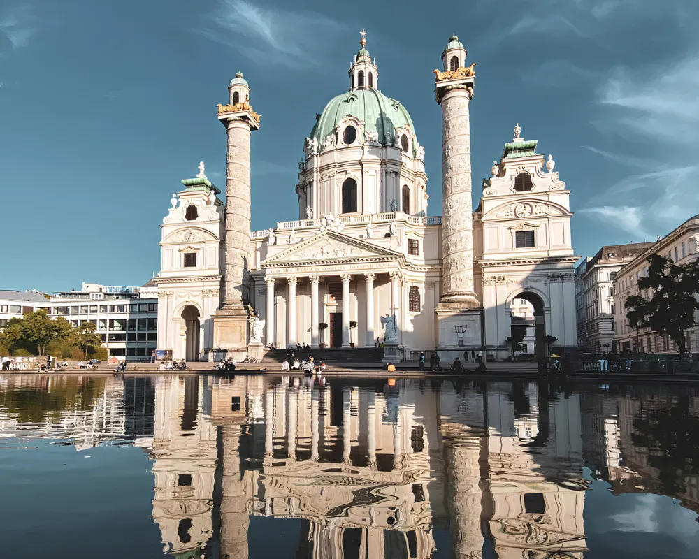 Viyana'da gezilecek önemli yerlerden barok mimarinin göz alıcı bir örneği olan Karlskirche, masmavi gökyüzü altında, önündeki havuzun sakin sularına yansıyan görkemli görüntüsüyle Viyana seyahat rehberi için büyüleyici bir başlangıç sunuyor.