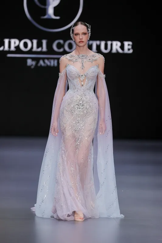 Transparan tül üzerine gümüş işlemelerle bezeli, omuzları açık ve pelerin detaylı, büyüleyici bir haute couture gelinlik tasarımı