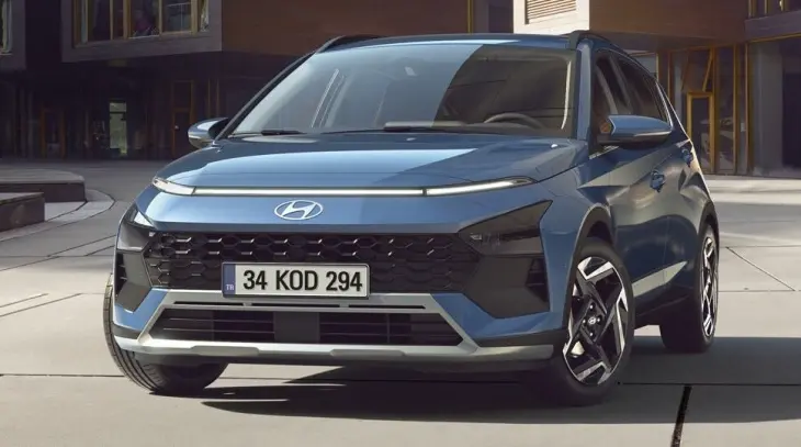 Mavi renkte bir Hyundai Bayon model araba, modern bir binanın önünde duruyor. Aracın ön paneli, farları ve parlak detayları belirgin bir şekilde görülüyor.