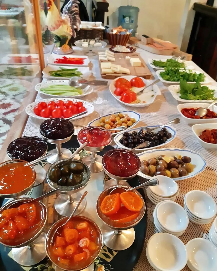 Büyük bir masanın üzerinde Alaçatı'nın en iyi kahvaltı mekanlarından birine yakışır şekilde, gümüş kaselerde incir, vişne, portakal kabuğu reçeli gibi bol çeşitli ev yapımı reçeller, taze yöresel peynirler, siyah ve yeşil zeytinler, dilimlenmiş domatesler, salatalıklar ve taze yeşilliklerle dolu zengin bir Türk kahvaltısı sergileniyor.