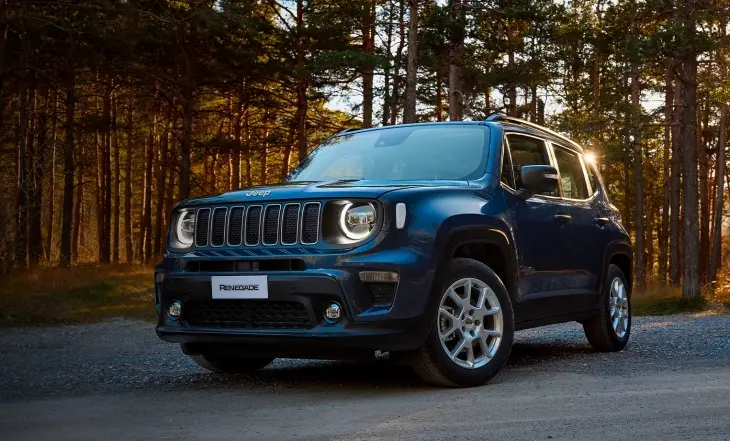 2024 model lacivert Jeep Renegade, gün batımı ışığında, ağaçlarla çevrili toprak bir yolda park halinde. Görsel, aracın karakteristik ızgarasını, yuvarlak LED farlarını ve araziye uygun, sağlam duruşunu ön plana çıkarıyor. Ön plandaki bu SUV, maceracı ve doğa sever kullanıcılar için ideal bir seçenek olduğunu yansıtıyor.