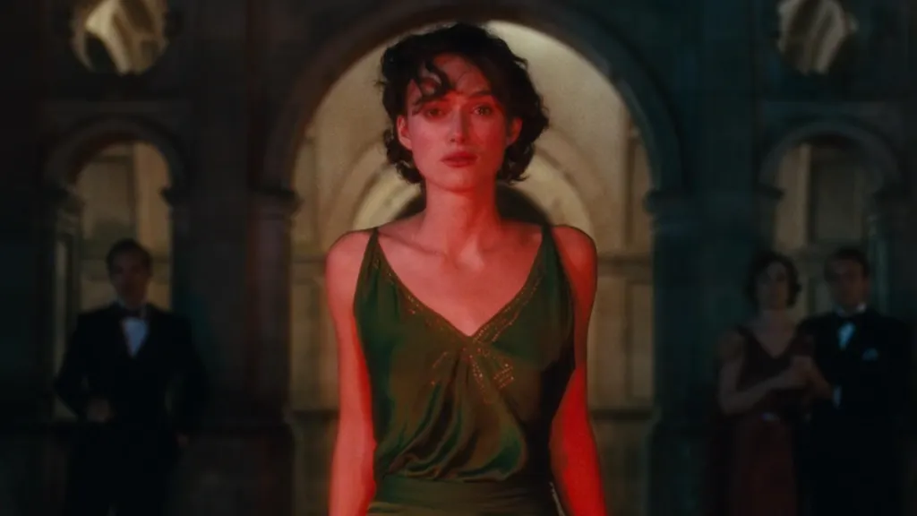 Kefaret (Atonement) filminden unutulmaz bir sahne: Yeşil elbisesiyle Cecilia karakteri (Keira Knightley), görkemli bir binanın önünde kırmızı ışıklar altında duruyor. Yüzündeki duygusal ifade sahnenin dramatik tonunu yansıtıyor, arka planda ise şık giyimli davetliler siluet halinde görünüyor.