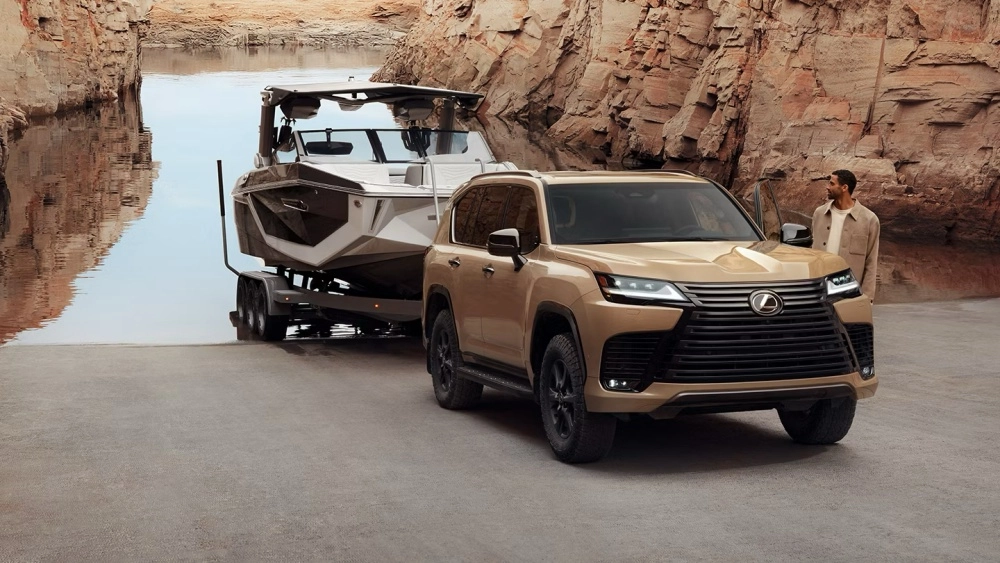 Kum rengi bir Lexus LX 700, geniş ön ızgarası ve dinamik dış mekan tasarımıyla dikkat çeken 7 kişilik lüks SUV olarak, kayalık bir koyda teknesini suya indirmeye hazırlanırken bir adam tarafından inceleniyor.