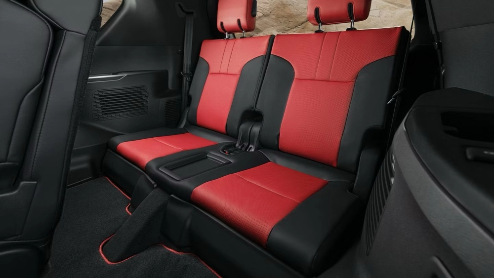 Lexus LX 700 lüks SUV modelinin iç mekan tasarımını gösteren bu görselde, kırmızı delikli ve siyah deri kombinasyonlu, yanlardaki havalandırma ızgaraları ve kırmızı şeritli paspaslarla tamamlanan, özenle tasarlanmış üçüncü sıra koltukları net bir şekilde görülüyor.