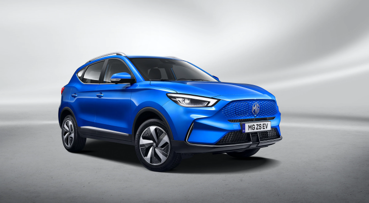 Mavi renkte bir MG ZS EV model elektrikli SUV, gri ve beyaz tonlarda bir stüdyo fonunun önünde duruyor. Aracın ön panjuru, şık jantları ve far detayları belirgin bir şekilde görülüyor.