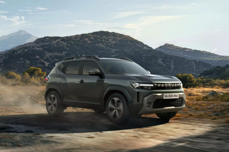 Yol dışında ilerleyen koyu renkli bir Renault Duster model araba. Arka planda kuru otlar, ağaçlar ve dağlık bir arazi manzarası görünüyor.