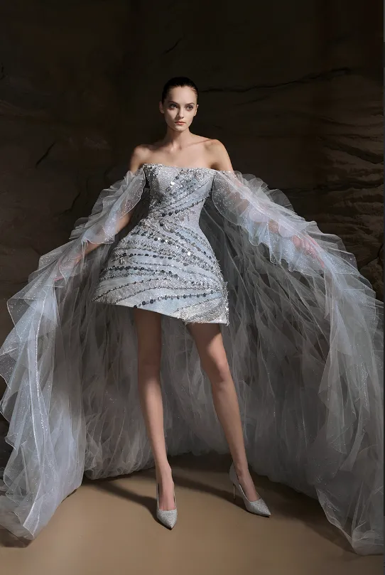 The Atelier 2025 İlkbahar koleksiyonundan, taş işlemeli mini elbise formunda tasarlanmış ve dramatik tül pelerinle tamamlanmış modern gelinlik modeli. Işıltılı detayları ve couture havasıyla nikah sonrası parti görünümü için iddialı bir tercih.