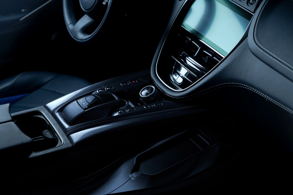 Aston Martin DBX 707 lüks SUV modelinin koyu mavi iç mekanından; dijital ekranı, şık havalandırma ızgaraları, karbon fiber detaylı orta konsol ve ergonomik vites kontrol düğmeleriyle dikkat çeken modern ön konsol tasarımı.