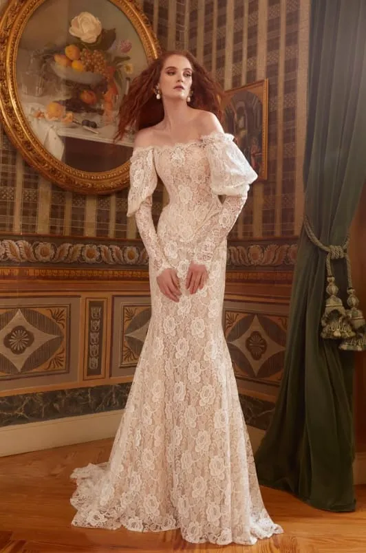 Kırmızımsı kahverengi saçlı bir kadın, zarif Galia Lahav imzalı, omuzları açık, uzun kollu ve tamamı dantel işlemelerle süslenmiş, alt kısmı genişleyen iddialı bir balık gelinlik modeli ile lüks bir salonda poz veriyor.