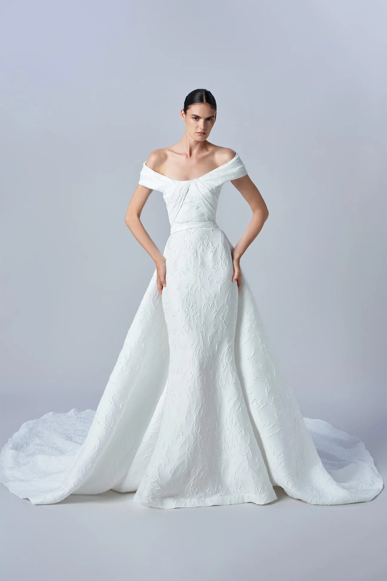 Elie Saab düşük omuzlu, göğüs kısmı büzgülü, tamamı kabartmalı floral desenli kumaştan üretilmiş, belden eklenen hacimli pelerin etekli balık model gelinlik.