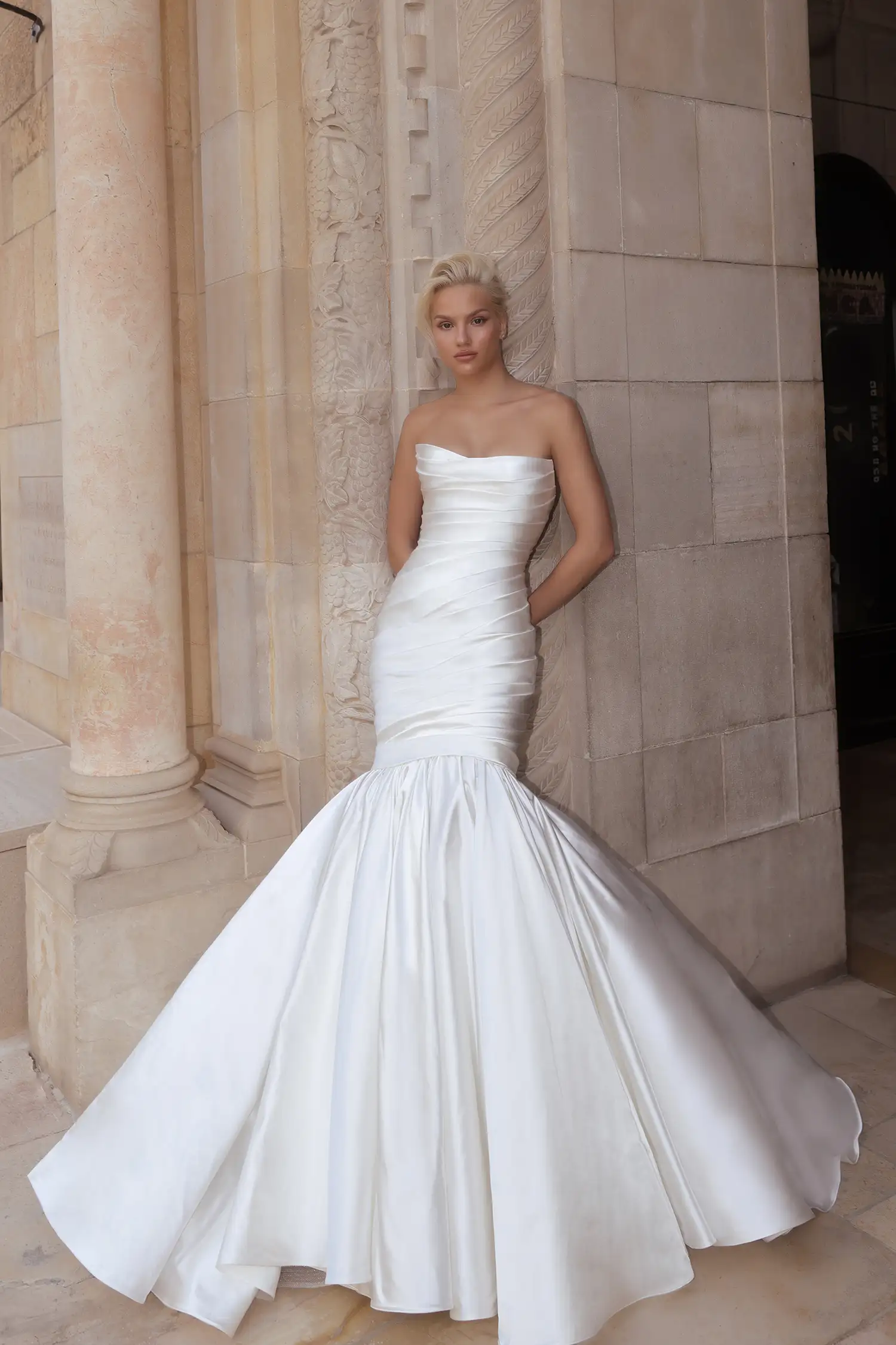 Pnina Tornai straplez düz yaka, gövdesi asimetrik drapeli ipek saten kumaştan, diz hizasından itibaren genişleyerek açılan hacimli kloş etekli balık model gelinlik.