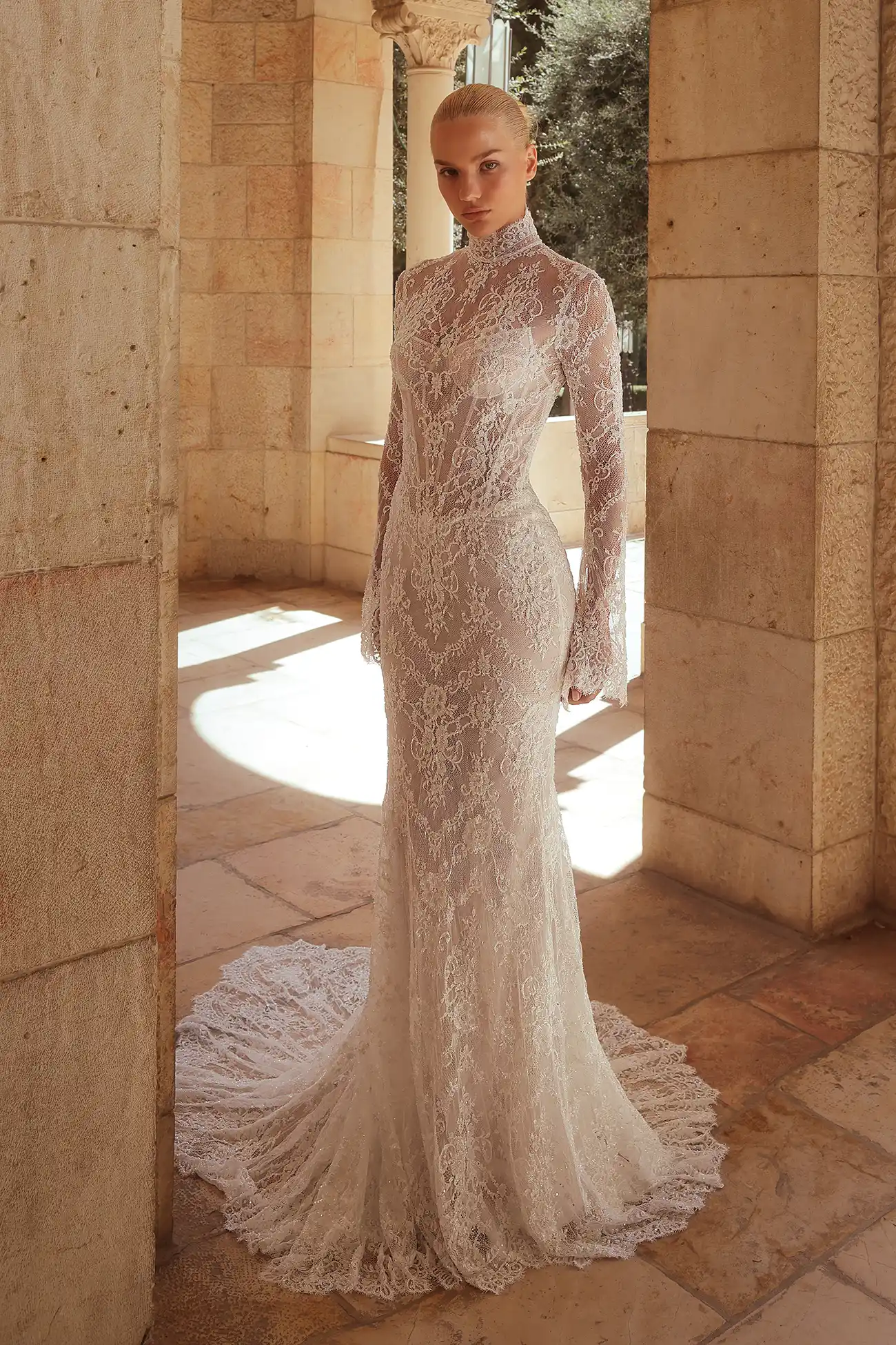Pnina Tornai yüksek hakim yakalı, uzun kollu, tamamı transparan efektli ince floral dantel işlemeli ve arkaya doğru uzanan zarif dantel kuyruklu balık model gelinlik.