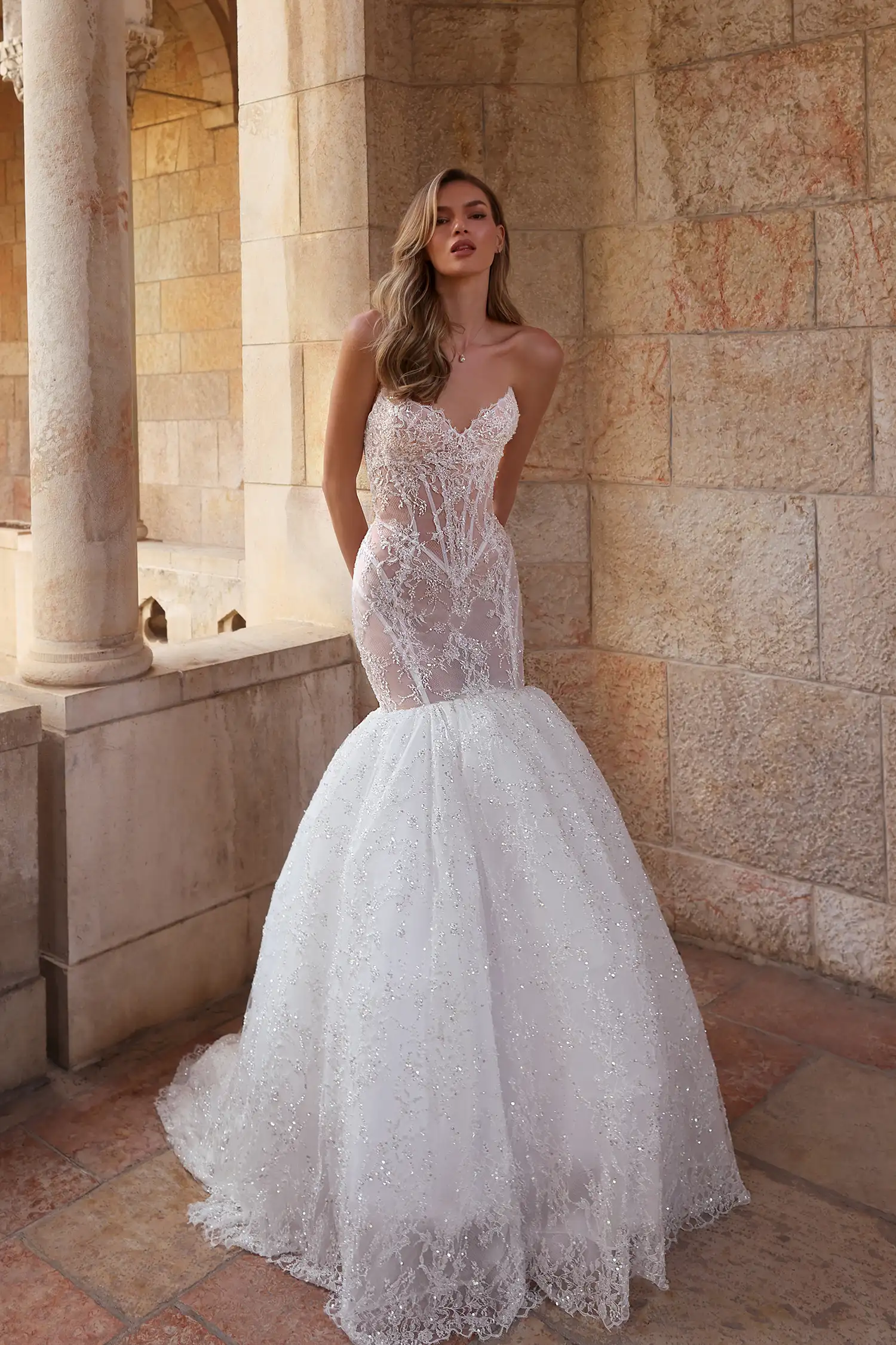 Pnina Tornai straplez kalp yaka, gövdesi transparan korse yapısında ve yoğun dantel işlemeli, diz üstünden itibaren aniden genişleyen hacimli ve ışıltılı tül etekli balık model gelinlik.