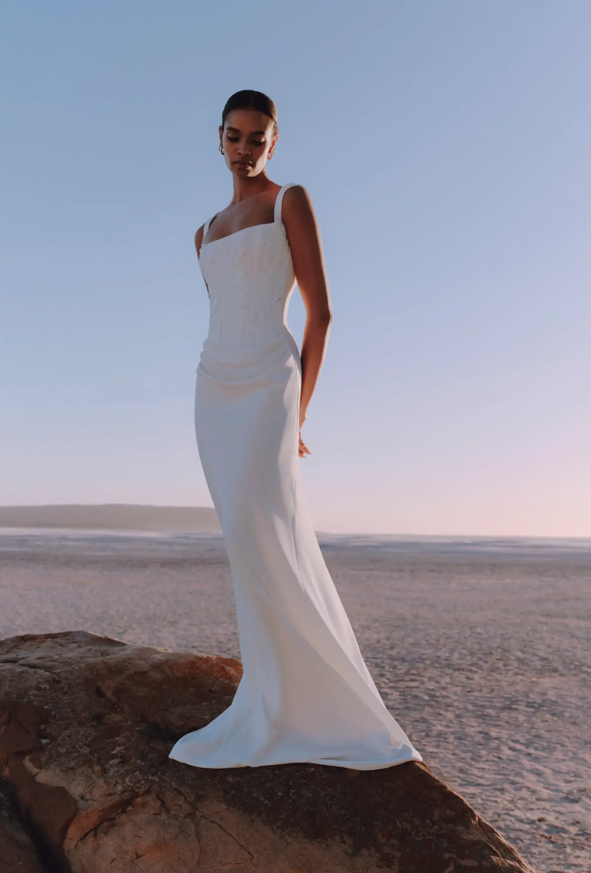 Project Bridal kare yaka, kalın askılı, gövdesi zarif beyaz işlemeli korse büstiyer formunda ve kalça hattında hafif drapeli geçişi olan krep kumaş balık model gelinlik.