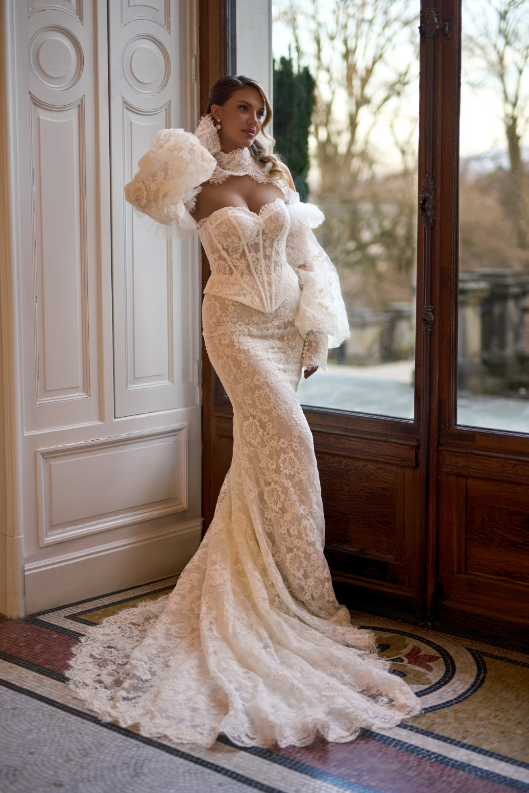 Sima Couture kalp yaka, gövdesi transparan balenli korse formunda, yüksek dantel yakalı bolero aksesuarı ve dramatik hacimli dantel kollarla tamamlanmış, tamamı Fransız danteli kaplı balık model gelinlik.