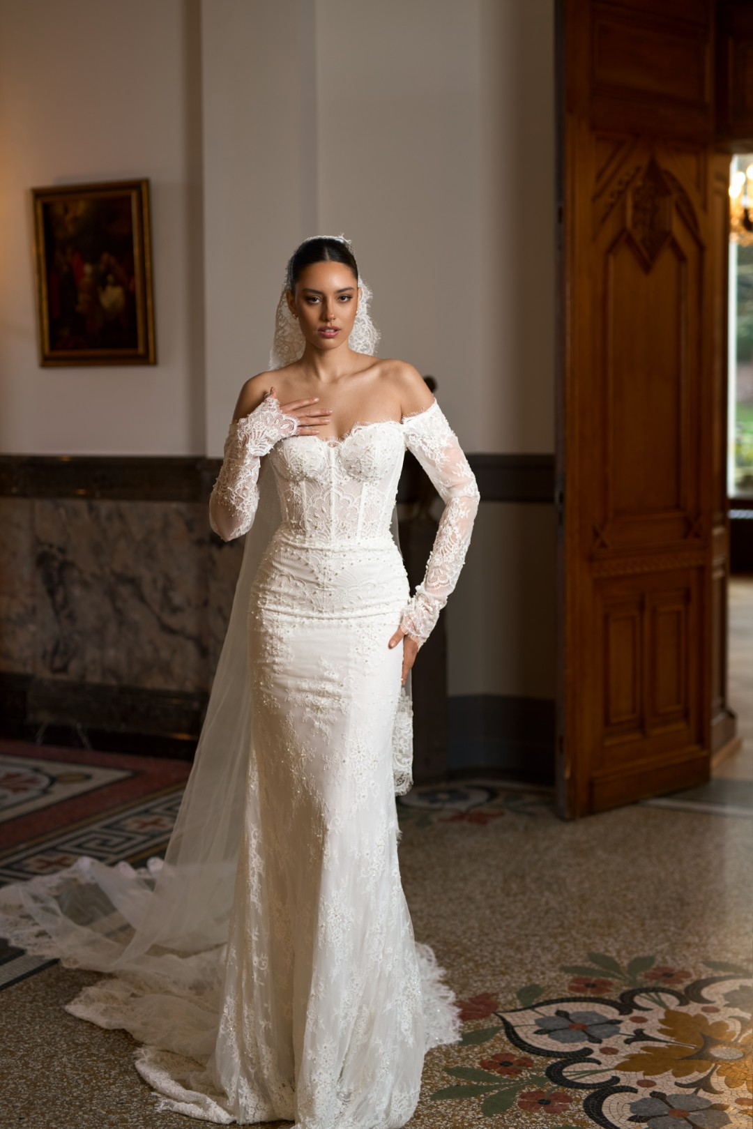Sima Couture düşük omuzlu, kalp yaka, gövdesi transparan balenli korse yapısında, parmak arası detaylı uzun dantel kollu ve etek uçları dantel işlemeli, uzun tül duvaklı balık model gelinlik.